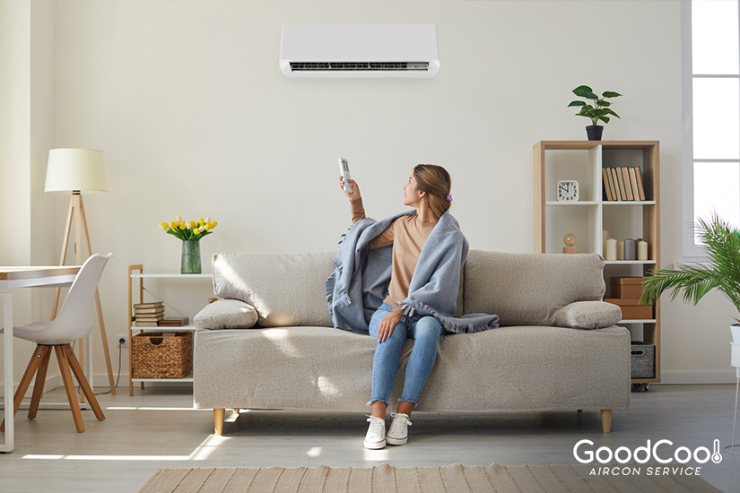 A woman adjusting a newly upgraded aircon system with a remote while sitting on a sofa.